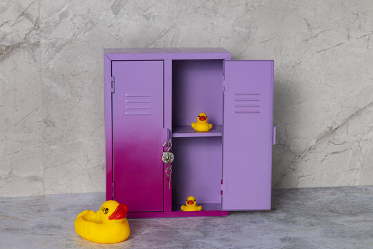 Small purple metal locker with open doors containing cute little yellow rubber ducks inside. Funny school storage concept, playful home organization decoration and abstract design