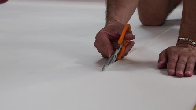 Person's hands carefully cutting white fabric with scissors