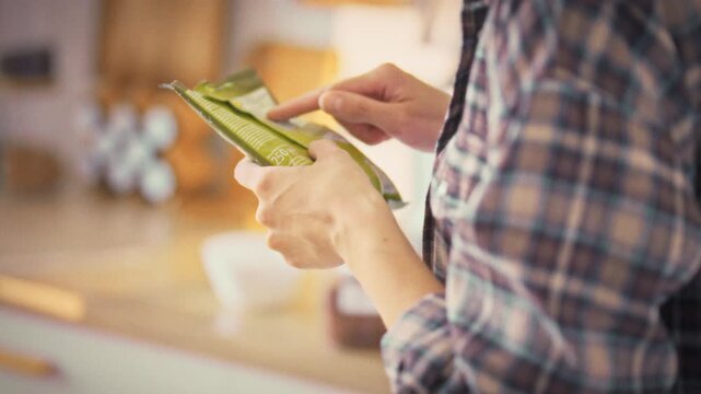 In kitchen, girl scans the ingredients on a product's plastic packaging, hunting for harmful additives. Her careful check underscores a focus on proper nutrition, food safety, and a healthy lifestyle