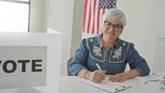 Woman signs ballot with hand at a voting table inside a public building, american flag on wall and clear ballot box on desk; civic duty pride.