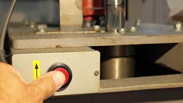 Operator's hand pushing red button on machine control panel