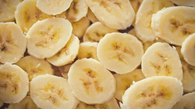Thinly sliced yellow bananas are piled in layered rows on a plate, creating a fruit surface that showcases a health-focused breakfast concept. The arrangement highlights nutritious, morning fare