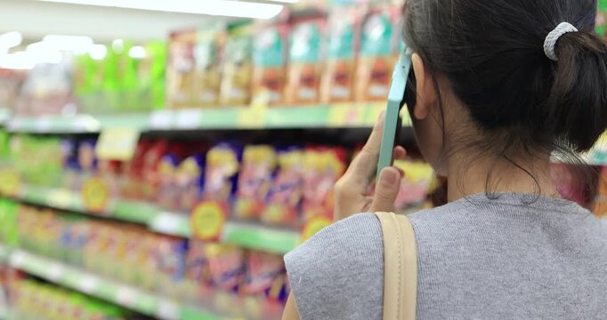 Woman talking on smartphone while shopping in a supermarket aisle. Consumer lifestyle, retail shopping, communication, grocery store, and everyday life concept, close-up