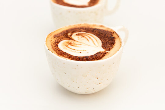 Caf&eacute; cappuccino avec un latte art coeur en gros plan sur une table blanche