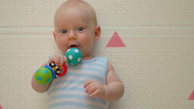 Three month old baby holding rattle and smiling at camera.