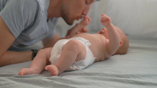 Father listening to baby sounds and kissing his infant son's hands.