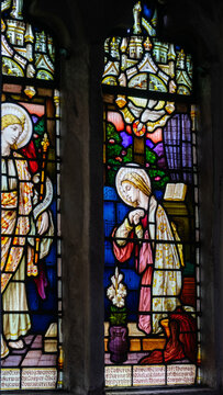 Stained-glass window depicting the Annunciation. The Virgin Mary is shown bowing in prayer beside a lily and an open book infront of Archangel Gabriel