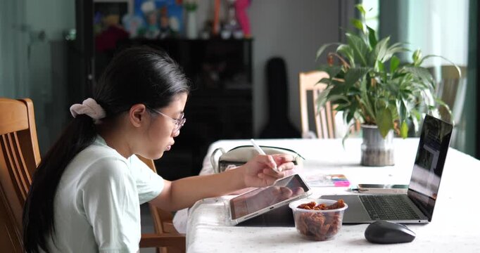 Side view of Asian teen girl studying online with digital tablet at home