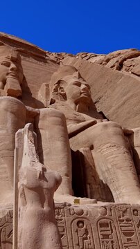 Close-up of giant Ramesses II colossi carved into rock facade at Abu Simbel temple, Egypt. Dramatic upward view of ancient sandstone pharaoh statues. Travel and history.