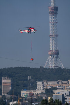 Firefighting helicopter of State Emergency Service with water bucket flying past TV tower in Kyiv Ukraine