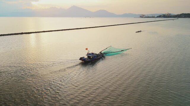 Fishing boat casting net on calm waters of da nang bay, vietnam, with distant mountains and city lights, reflecting warm sunset glow on traditional seascape and maritime activity