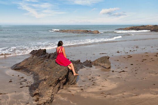 Woman in red dress relaxing by the sea at Vagator Beach, in North Goa, India