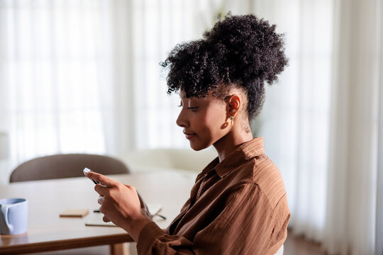 Woman with curly hair checking smartphone during work break at desk