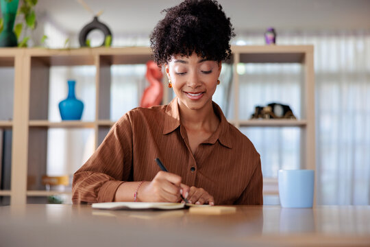 Woman writing in notebook at desk, smiling.