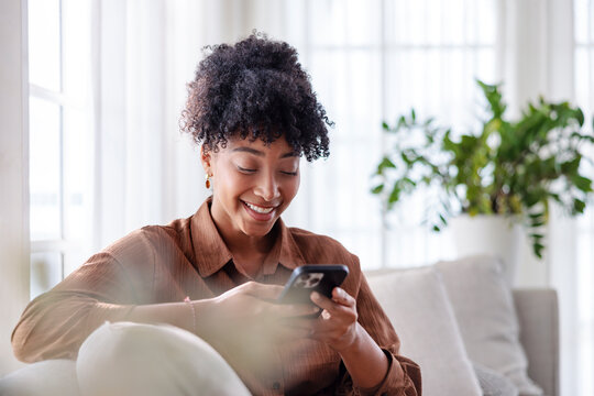 Woman smiles while using her mobile phone on a couch.
