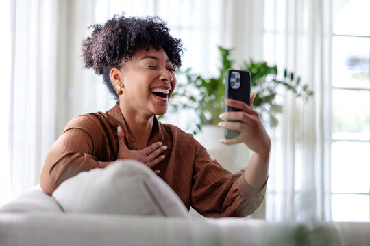 Laughing woman enjoying video call from couch in cozy home setup