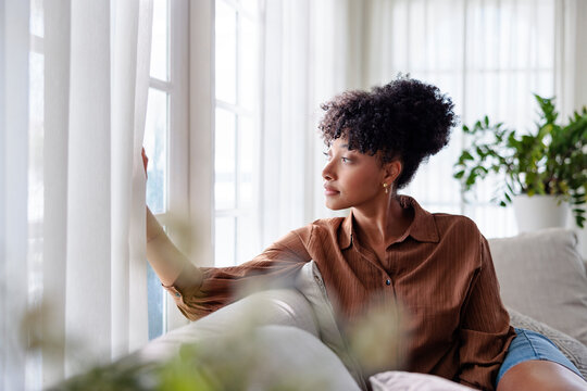 Thoughtful woman looking through window in cozy living room