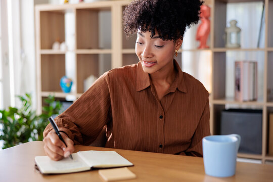 Woman writing in notebook at desk with mug.