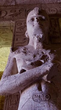 Symmetrical row of colossal Ramesses II osiride pillars lining both sides of main hall at Abu Simbel temple, Egypt, faded painted ceiling with vultures above.