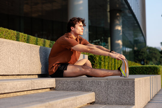 Man stretches leg on steps near modern building.