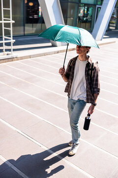 Man with umbrella and water bottle in urban setting.