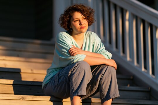 Young woman sitting on wooden steps in warm evening light for relaxed lifestyle background and portrait banner use
