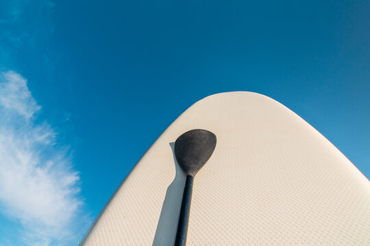 White SUP board with paddle against blue sky