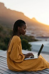 Naklejka premium Young woman on a deck using laptop at sunset in a yellow dress for remote work background and website banner design