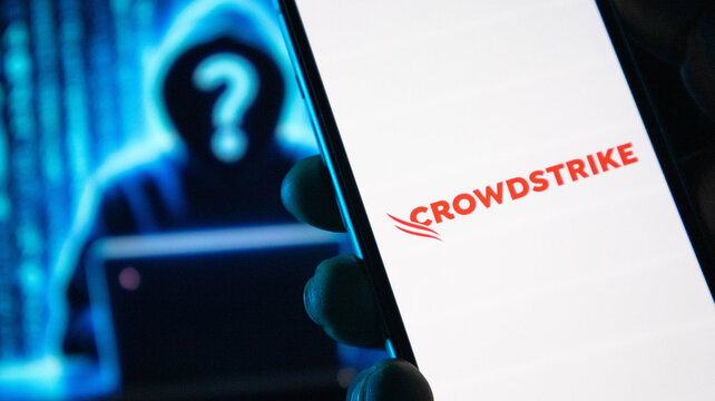 Smartphone displaying crowdstrike logo against blurred hacker background with binary code.