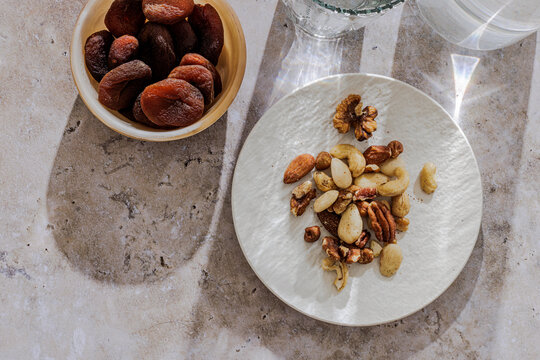 Nuts on a plate and apricots in a bowl on a stone surface