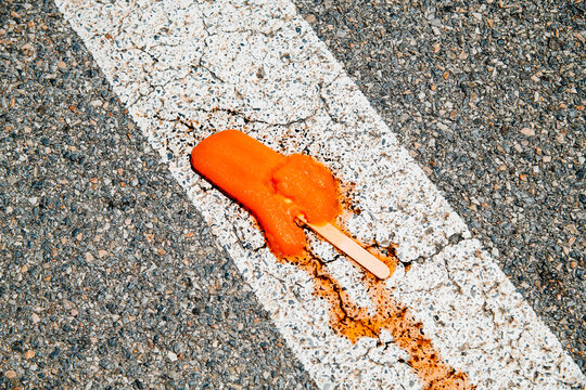 an orange ice pop melts on a worn road marking