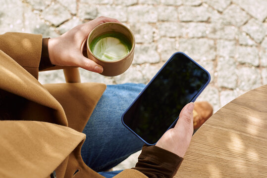 Person holds a phone and drink in outdoor setting