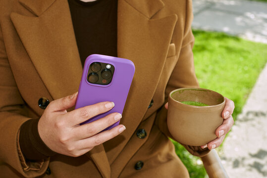 Person holds phone and cup in outdoor setting
