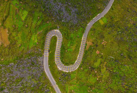 Aerial view of a winding serpentine road cutting through the lush green mountainous landscape with rocky outcrops and vibrant vegetation in Dong Van, Tuyen Quang, Vietnam.