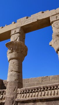 Dramatic upward view of ornate papyrus columns with carved floral capitals and stone lintels at Philae temple, Aswan, Egypt, against vivid deep blue sky.