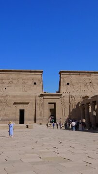 Tourists exploring the Philae Temple complex under clear blue sky, showcasing ancient Egyptian architecture, courtyards, and well-preserved stone structures.