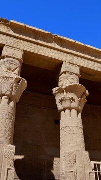 Upward view of ornate floral capitals on Ptolemaic columns at Philae Temple, Aswan Egypt. Elegant ancient architecture against vivid blue sky. Travel and history content.