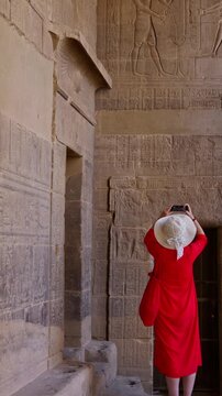 A woman in a red dress examines the ruins of the Philae Temple, Aswan, Egypt.