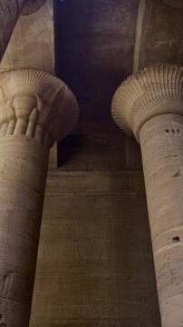 Ancient Egyptian Philae Temple. interior with massive carved stone columns covered in hieroglyphs, low angle view highlighting detailed reliefs and architectural grandeur.