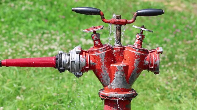Flowing water escaping from a red fire hydrant valve in an urban environment, slow motion