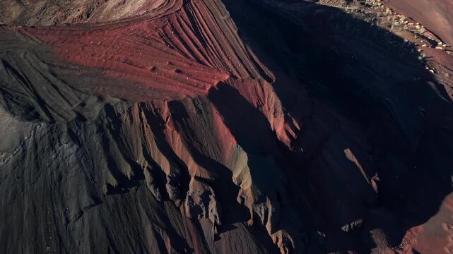 An aerial close-up drone shot focusing on the dramatic textures, eroded ridges, and sharp color contrast between black basalt ash and red iron oxide slopes of a volcanic crater in El Pinacate, Mexico.