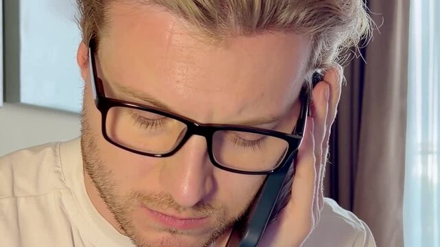 Close-Up of a Young Man Working on a Laptop, Wearing Glasses with the Screen Light Reflecting in His Lenses