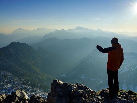 Climber at the summit of Krn 2. 244m pointing to his next target, Triglav National Park, Julian Alps, Slovenia