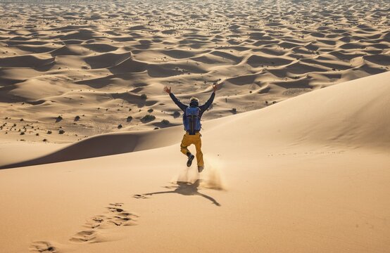 Young man walking down a sand dune, dune landscape Erg Chebbi, Merzouga, Sahara, Morocco