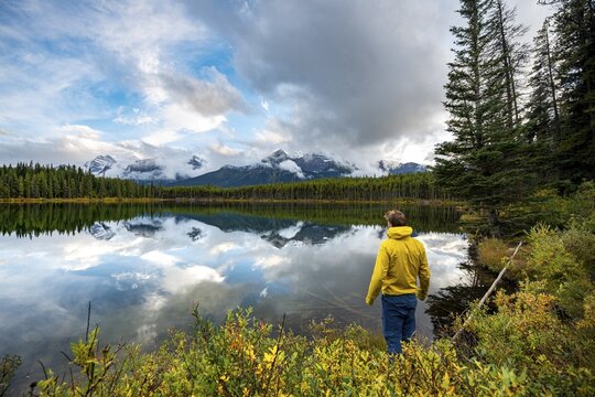 Hiker at the lakeside looking at mountains, autumnal Herbert Lake, mountains of the Bow Range reflected in the lake, Banff National Park, Canadian Rocky Mountains, Alberta, Canada