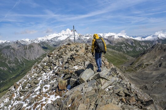 Mountaineers at the summit of B&ouml;ses Weibl with summit cross and colourful prayer flags, view of picturesque mountain landscape with snow-covered summit of the Gro&szlig;glockner, Wiener H&ouml;henweg, Schober group, Hohe Tauern National Park, Carinthia, Austria
