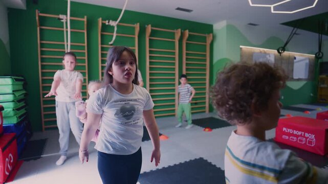 Children actively participates in a fitness class, performing various balance and coordination exercises. Kids are seen focusing on their movements and developing physical skills in a gym setting.
