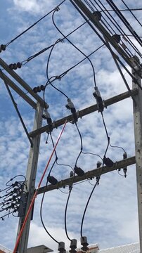 Low angle video of a worker using an insulated fiberglass hot stick to close high voltage drop out fuse cutouts phase by phase on a concrete transformer pole structure.