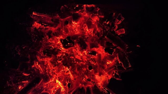 Close up of glowing charcoal embers burning with red and orange tones at night. Soft heat and shimmering texture create magical atmosphere. Warm abstract scene symbolizing warmth and quiet at nature