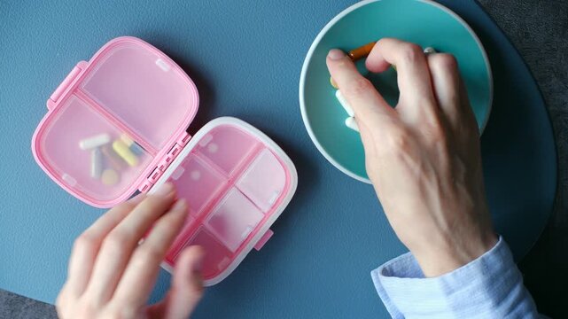 Top view female hands carefully sorting, placing various colorful pills, capsules, vitamin supplements from plate in daily pill organizer, medication management. Person sorting pills in organizer box